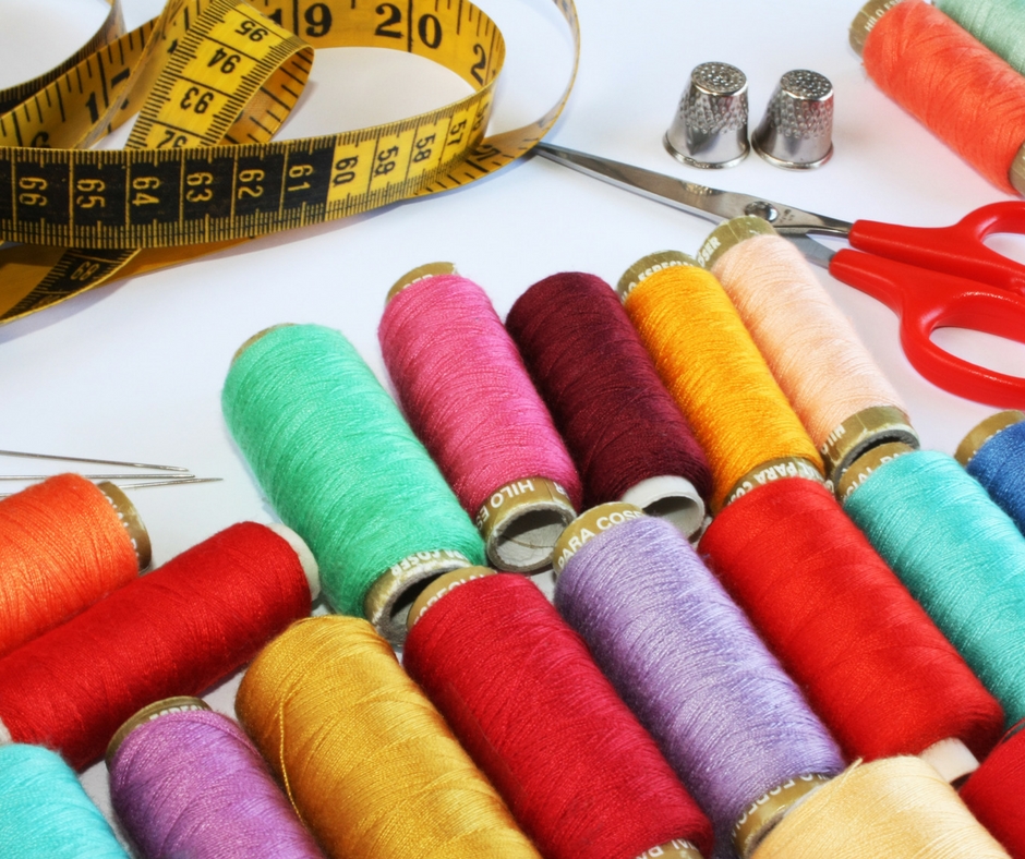 Numerous thread spools, thimbles, a pair of scissors an measuring tape