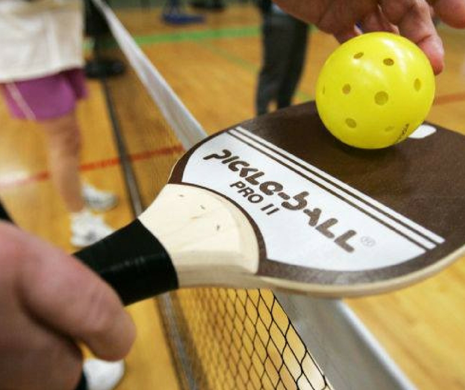 Pickleball paddle holding a yellow ball above a net