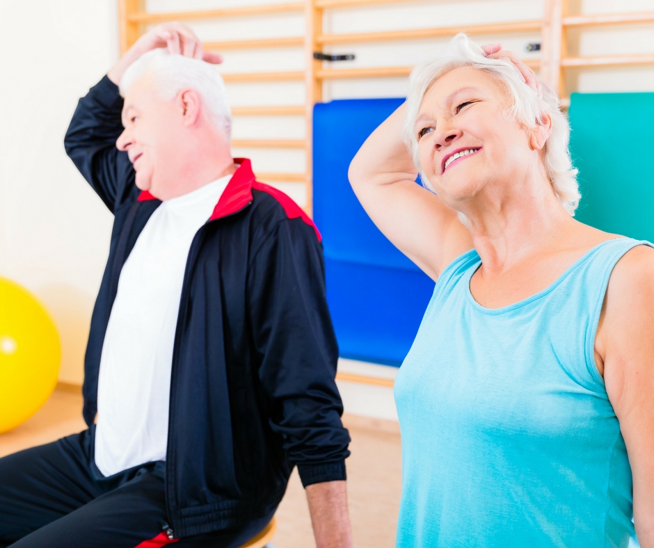 One male and one female senior citizen sitting on chairs and stretching.