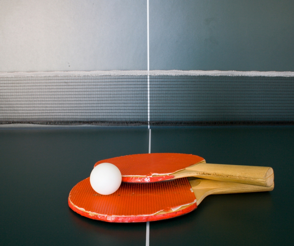 Two red paddles and one white ping pong ball laying on a green ttable tennis table.