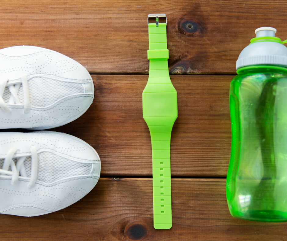 A pair of white sneakers, green fitbit and green water bottle on gym floor