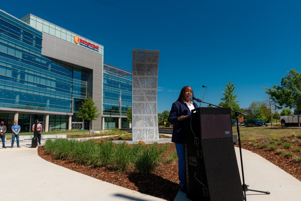 Woman speaks at podium in outdoor park.