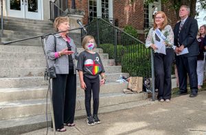 A woman stands behind a microphone with a female child. Over to the right is another woman and Mayor Tommy Battle