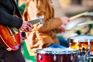 Festival music band. Hands playing on percussion instruments in city park . Drums with sticks closeup. Body part of male musicians. Sharpen is guitar and man hand