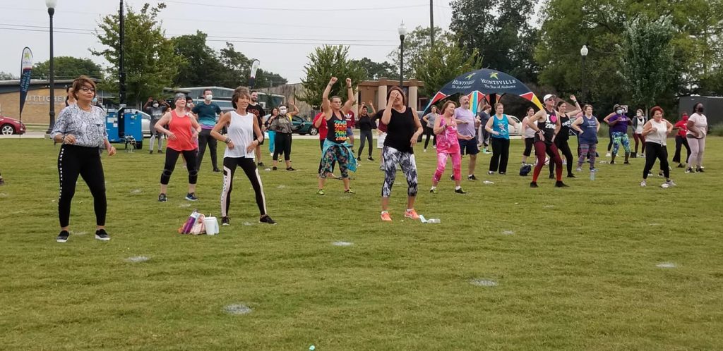 Dozens of people dancing outside on a green lawn.