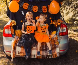 girls dressed up for Halloween with orange jack-o-lantern buckets trunk or treat