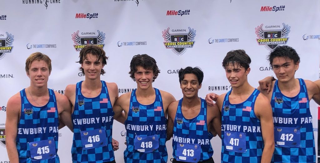 Runners posing in front of finish line graphics at an outdoor event.