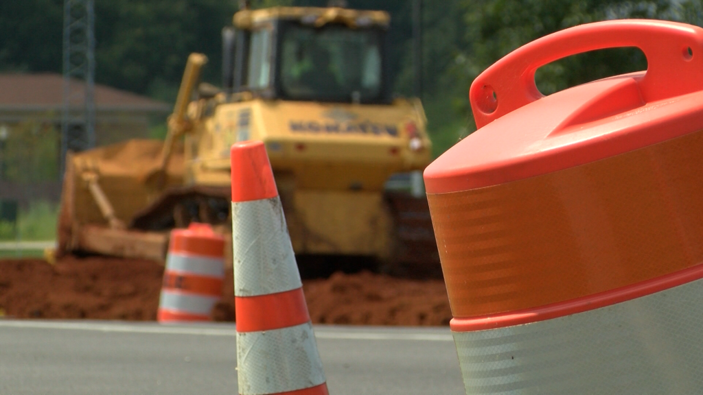 orange and white striped construction cones and barrels in front of a bulldozer pushing dirt alongside a road