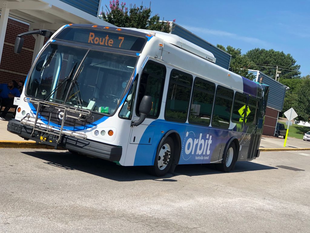 An Orbit bus is seen at a stop next to a building.