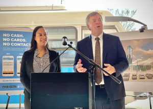 Huntsville Mayor Tommy Battle and Parking and Public Transit Director Quisha Bryant announce the official launch of Token Transit March 30 at the Huntsville Transit station. There are posters of the Token Transit app and a rendering of the new transfer station behind them.
