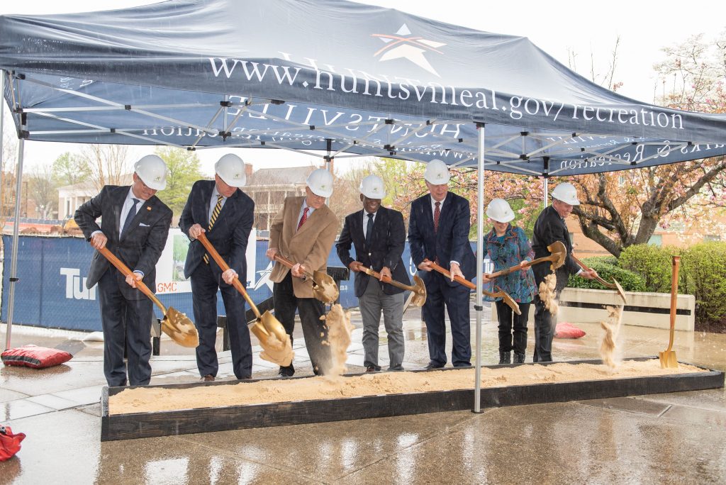 leaders in hard hats shovel sand at groundbreaking