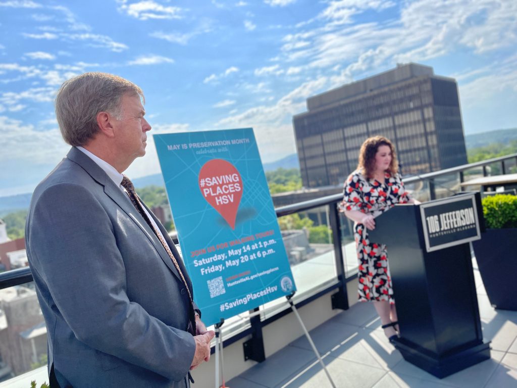 man stands while woman speaks at podium on rooftop