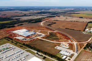 An aerial view of Huntsville's western industrial corridor. There is a lot of red dirt and a large building under construction. There is flat farmland in the distance.