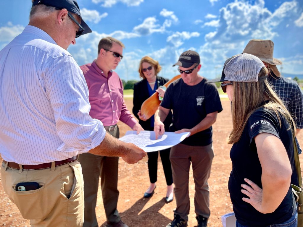 A group of people look at plans for a skatepark while standing in a dirt field
