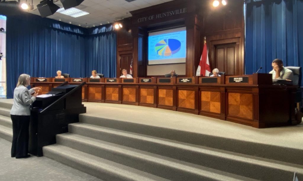 Finance Director Penny Smith stands at the podium in the Council Chambers to present Mayor Battle's budget to Council Members who are sitting on the dais.