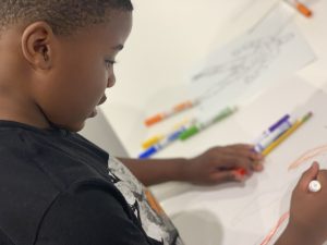 A young boy draws on paper using colored markers.