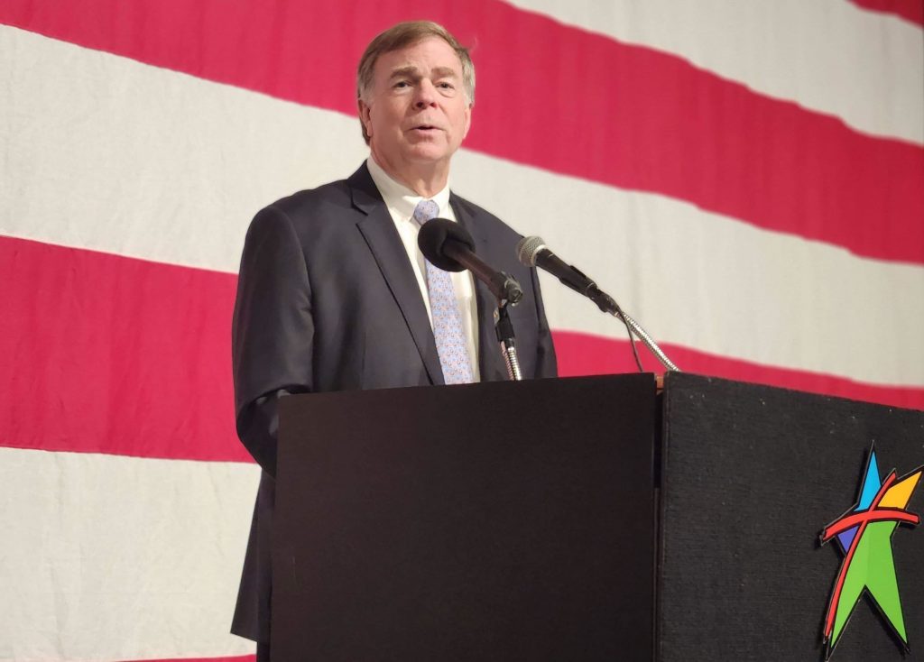 Mayor Tommy Battle delivers his 2022 State of the City address at a podium. There is a large American flag behind him in the background.