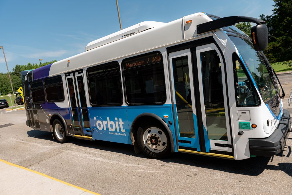 An orbit bus is seen next to a curb on a sunny day with blue sky.