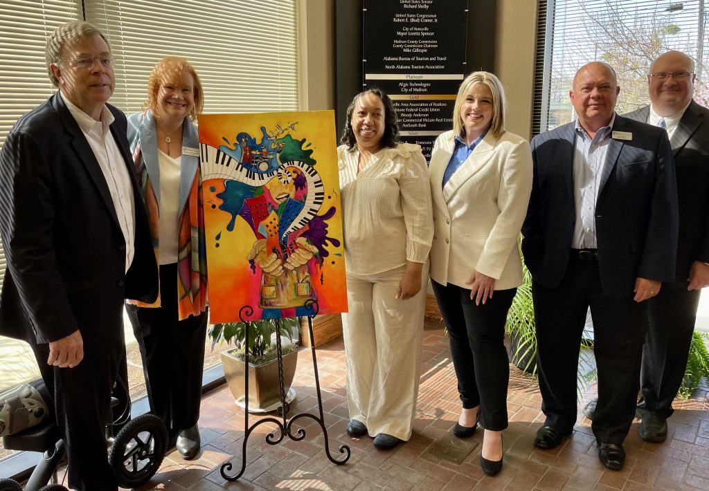 Mayor Battle stands next to a group of people showing a colorful graphic poster about Panoply designed by a local artist.
