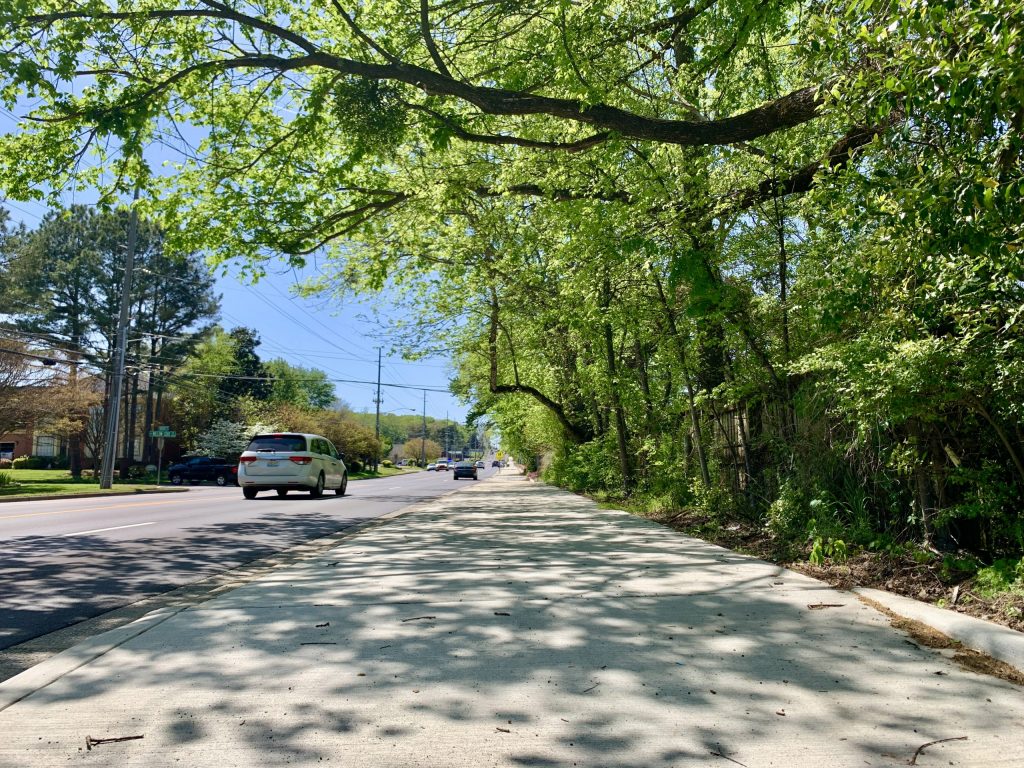 A sidewalk is seen next to a wooded area off Weatherly Road in south Huntsville. Cars can also be seen in the background.