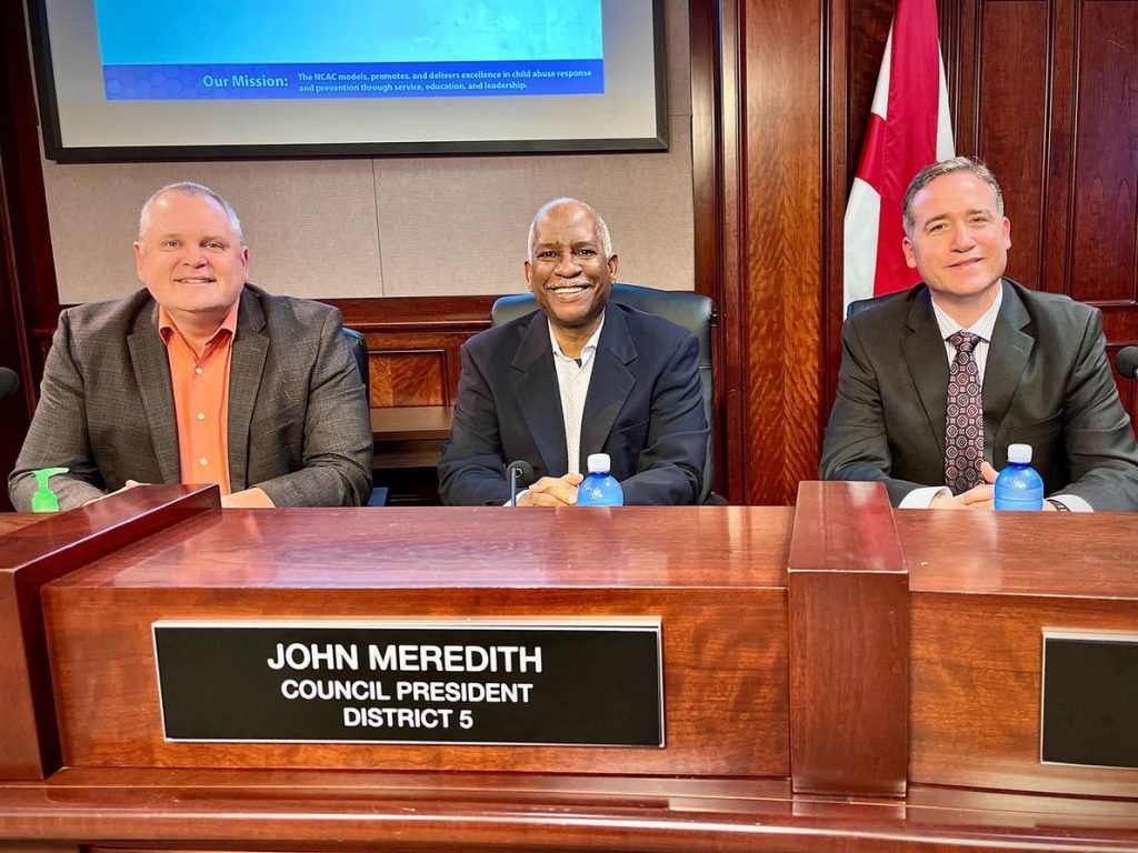 men smile for photo behind wooden dais in council chambers