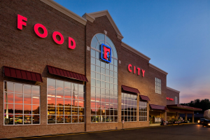 The exterior of a Food City is shown with an evening sky in the background. The letters are red and there is glass windows across the front of a brick building.