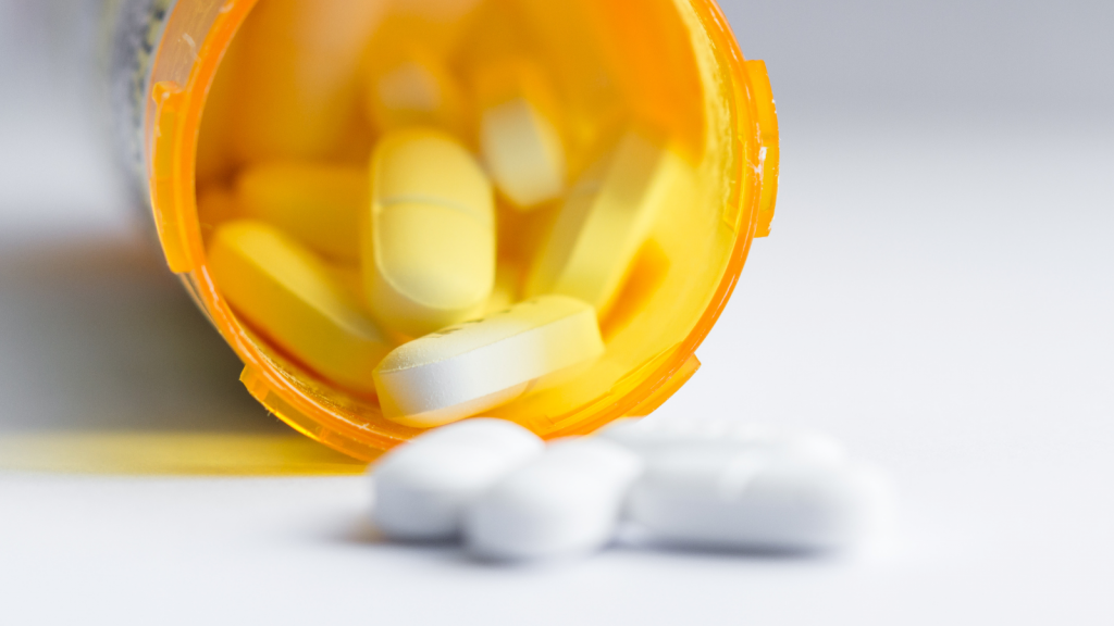 Pills spill out of an overturned pill bottle onto a white surface.