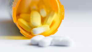 Pills spill out of an overturned pill bottle onto a white surface.