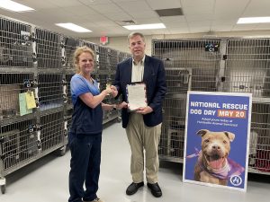 Mayor Tommy Battle presents a proclamation to Huntsville Animal Services Director Dr. Karen Sheppard. There are cat kennels in the background and a poster to the right.