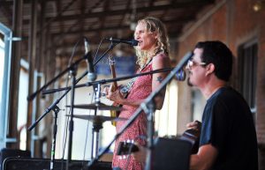 A music duo consisting of a standing woman and sitting man perform at a music festival.