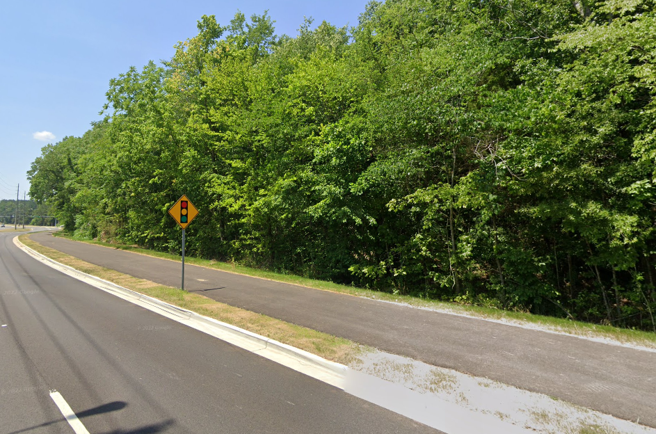 A photo of the Zierdt Multiuse path. To the left is Zierdt Road. To the right are many trees. There is a sign visible warning drivers of a traffic signal ahead.