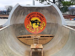 a bright orange and round logo with a dark image of someone on a skateboard is in the middle of a concrete pipe