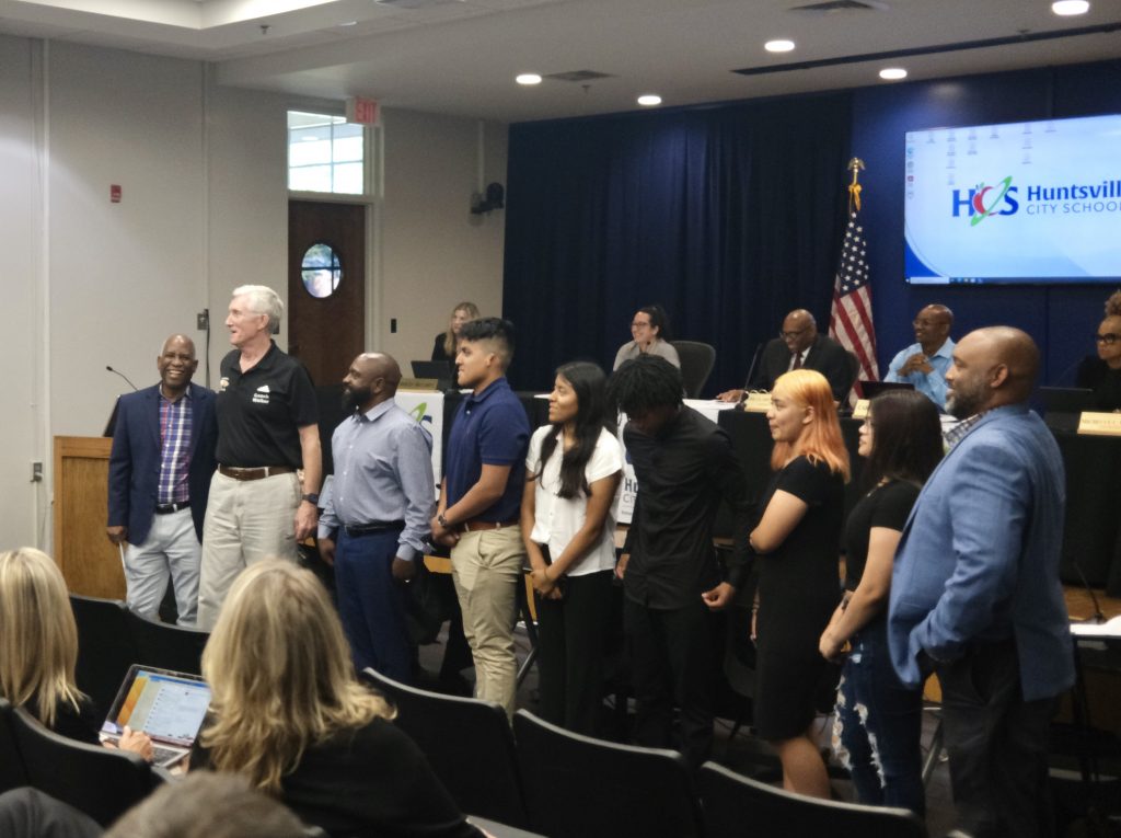 group photo of people standing in line in front of school board panel