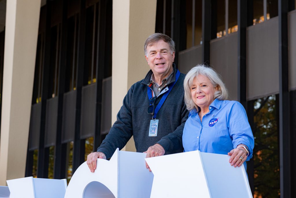 Man and woman smile behind white NASA sign