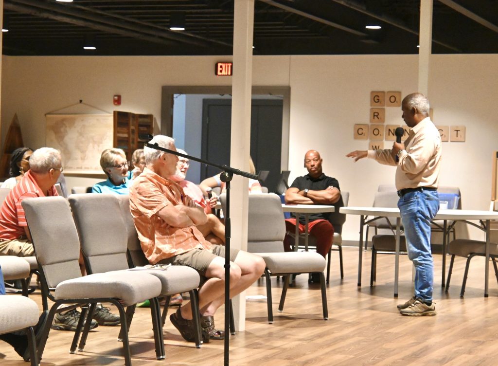 Man holding microphone speaks to adults sitting in chairs