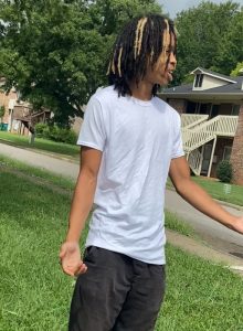Man wanted for capital murder with long hair looking at camera with white t-shirt another angle