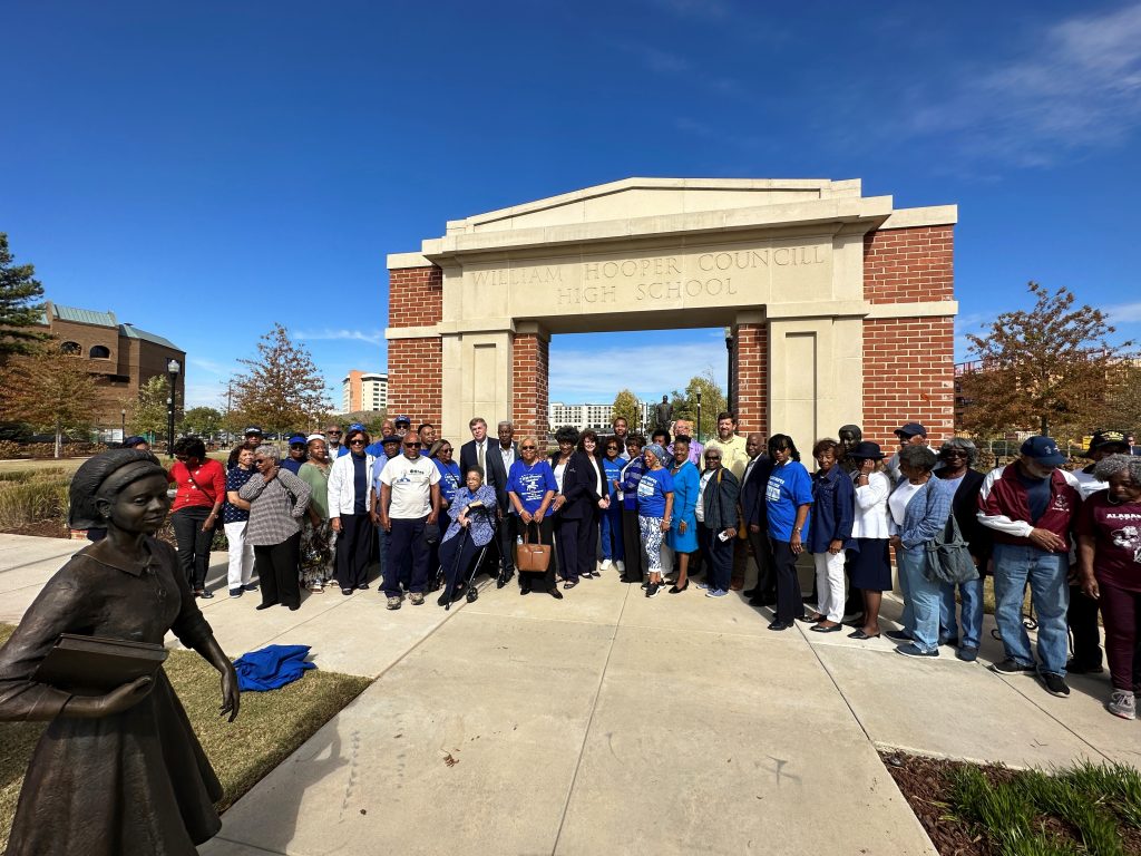 line of people standing outside in front of an arch and a statue in a park