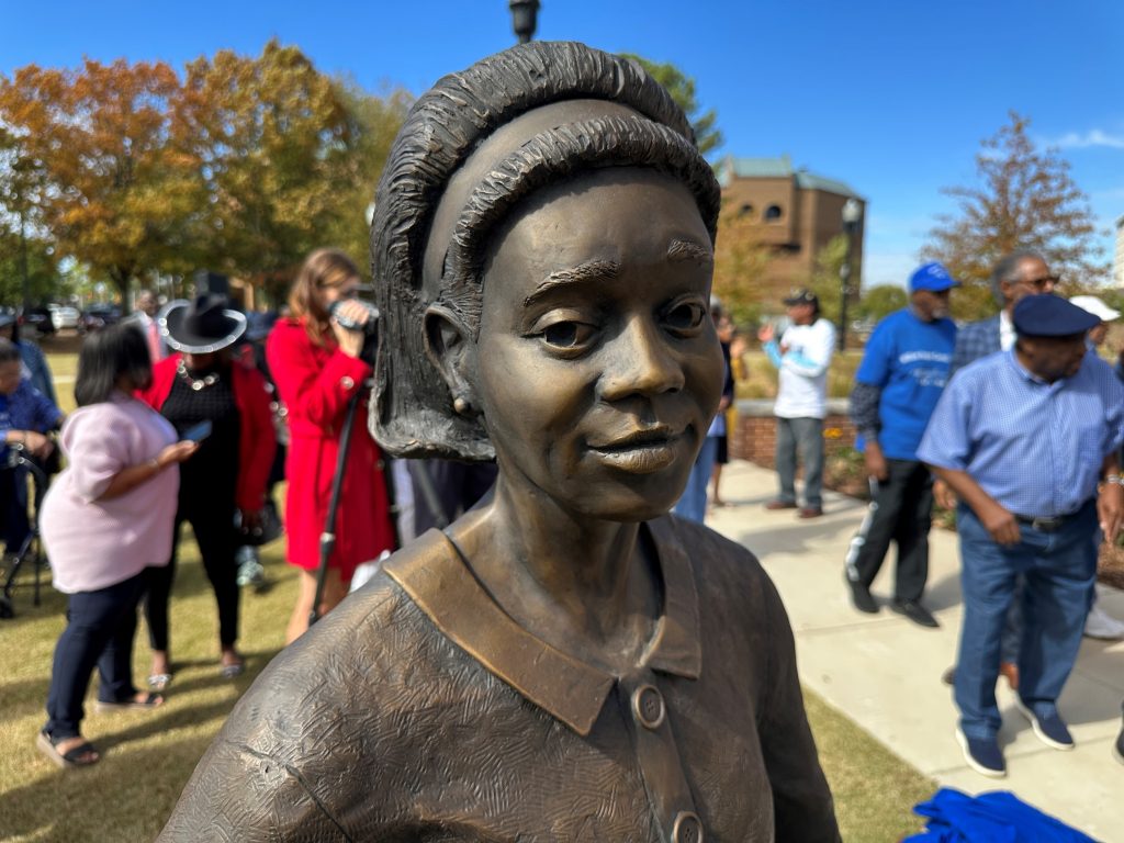 face of a girl in a bronze statue in an outdoor park with people gathered around