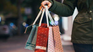 A woman carries Christmas packages in bags by their handles.