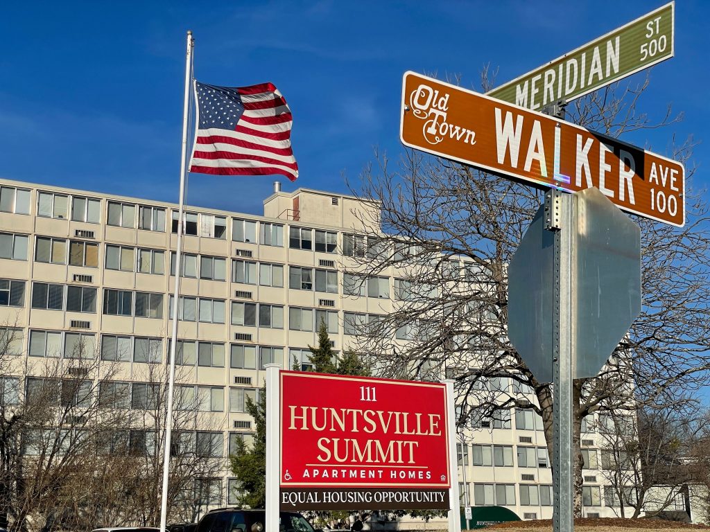 A photo of the Summit Apartments located in downtown Huntsville. There's an American flag to the left and street signs in the foreground.