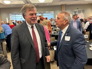 mayor battle, a man in a gray suit, laughs with another man in a gray suit in a room filled with people