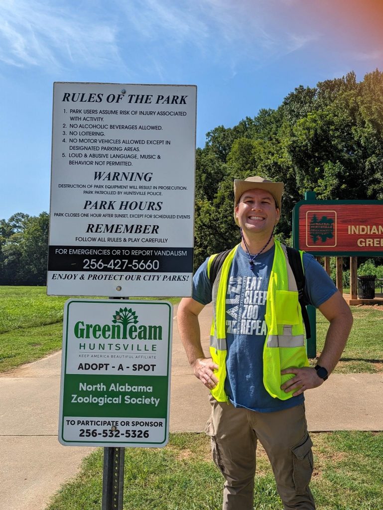 man wearing a yellow safety vest standing in front of an adopt a spot sign