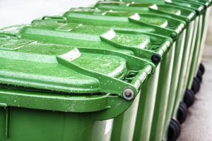 A line of green garbage carts in a row.