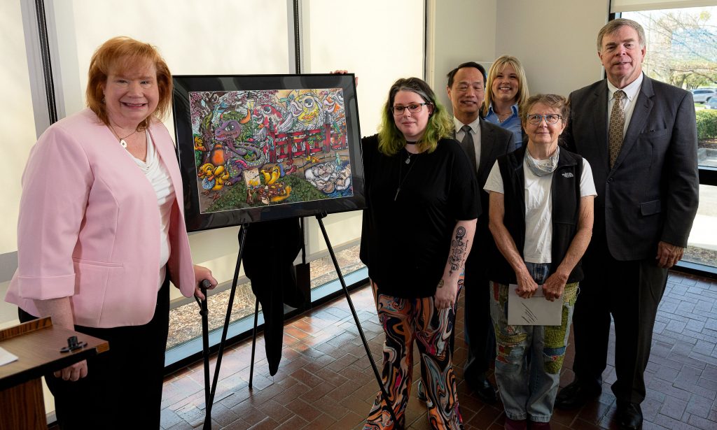 people standing in a line by an easel with artwork - a multicolor design showing fish, animals, and imaginary beasts in a park