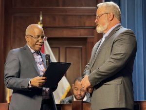 two men wearing jackets and glasses. one man presenting plaque to the other.