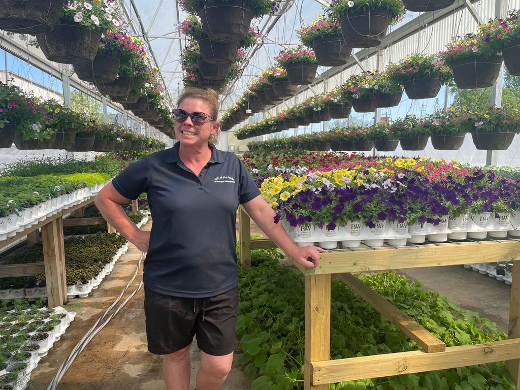 Woman in dark shirt standing in greenhouse surrounded by plants
