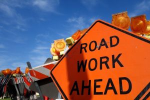 orange sign says road work ahead below blue sky