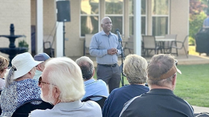 man standing in blue shirt speaking into microphone addressing audience