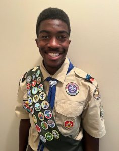 smiling african american boy wearing an eagle scout uniform and sash laden with badges he earned