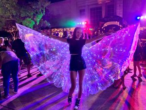 A young lady spreads her butterfly wings at the 2023 Light Up the Night in Big Spring Park East. There are colored lights all around her.